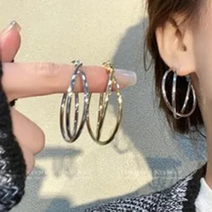 Detailed macro view of silver and gold interwoven hoop earrings worn on the earlobe