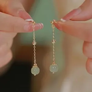 Close-up detail of elegant gold chain drop earrings featuring pale green round beads