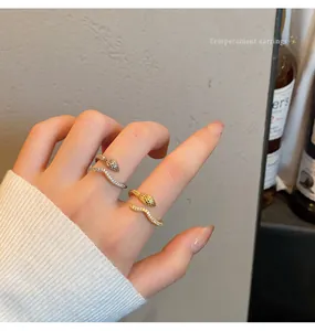 Close-up of gold and silver snake-shaped open rings with sparkling stones on hand.