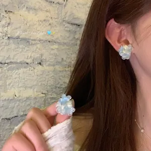 Detailed close-up showing clear blue gradient flower beaded earrings on a model's ear