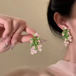 Detail shot of elegant pink floral cluster earrings with green leaves on model's ear