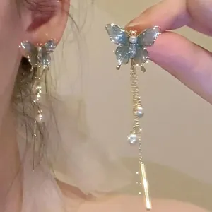 Close-up detail of blue butterfly tassel earrings with elegant pearls on an ear.