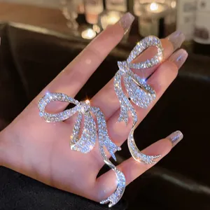 Close-up detail of sparkling rhinestone bow earrings with an asymmetric tassel design