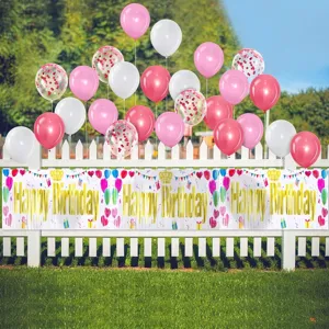 Happy Birthday foil fringe banner on a white fence with colorful balloons outdoors