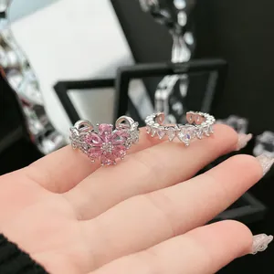 Nahaufnahme eines rosa Blumen-Zirkonia-Rings und eines silbernen Herz-Kristallbands am Finger