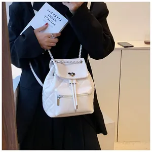 Détail d'un sac à dos blanc matelassé avec chaîne argentée porté avec un blazer noir