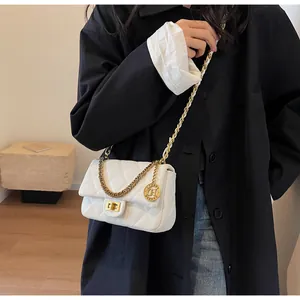 Primo piano di borsa a tracolla trapuntata bianca con catena dorata e ciondolo rotondo.