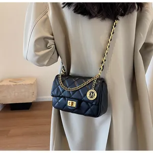 Dettaglio di borsa a tracolla trapuntata nera con catena dorata su cappotto beige