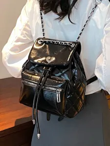 Sac à dos en cuir verni matelassé noir à bretelles de chaîne porté par un modèle