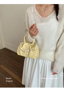 Macro view of stylish yellow pleated cloud handbag featuring an elegant beaded handle