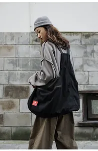Large black functional crossbody bag worn by a model in urban street style setting