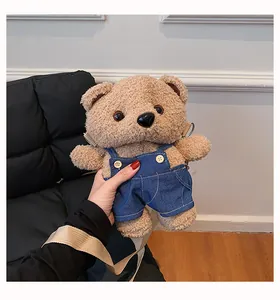Detail view of a cute brown plush teddy bear crossbody bag wearing blue denim overalls
