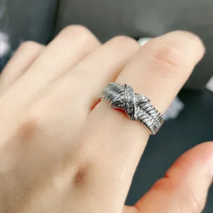 Close-up view of a silver ribbed X-shaped crossover ring with sparkling crystals on a finger