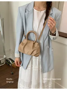 Stylish tan ruched cloud bag worn crossbody by a model with a light blue blazer