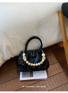 Close-up of black pleated cloud handbag with decorative beaded strap on lifestyle background.