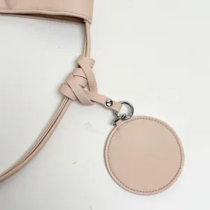 Close-up of pink leather bag detail with knotted strap and circular charm.