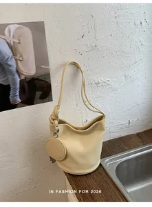 Detailed side view of cream minimalist bucket bag with round coin purse on wooden counter