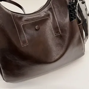 Dettaglio di borsa tote in pelle marrone scuro con cuciture a contrasto e foulard.