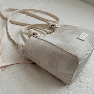 Close-up detail of a minimalist beige bucket bag featuring textured fabric and knotted handles