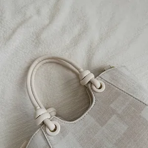 Detailed close-up of a beige canvas handbag showing the top handle and stitching