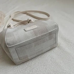 Detailed view of cream fabric bucket bag with refined stitching and brand patch