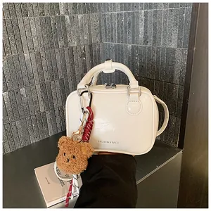 Detailansicht einer weißen minimalistischen Handtasche mit süßem braunem Bärenanhänger