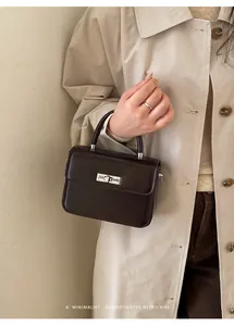 Close-up of dark brown minimalist leather handbag with silver clasp shown on trench coat