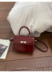Close-up of elegant burgundy leather square handbag with silver metal lock on floor