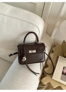 Macro view of a sophisticated glossy brown handbag featuring a silver heart charm and turn-lock