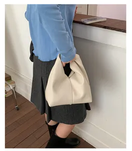 Side view of a white pebbled leather pleated bucket bag held by a model in casual outfit
