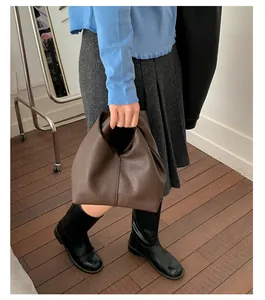Model carrying a brown pleated leather handbag with a minimalist textured finish and chic design