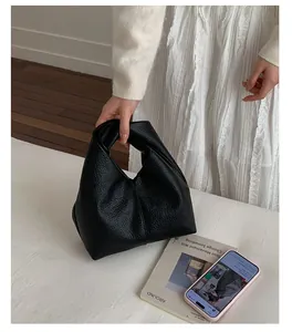 Close-up of minimalist black pleated leather handbag held by a female model