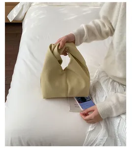Detailed view of a beige pleated handbag with a unique knot handle on a white bed