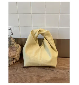 Close-up of a yellow pebbled leather knot handle handbag on a wooden surface.