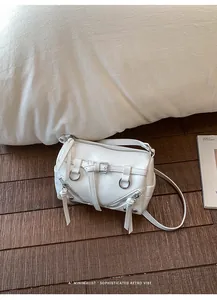 Detail view of a white minimalist pillow bag with zipper and buckle accents on wooden floor