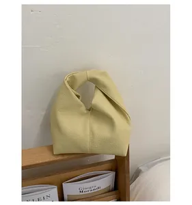 Detailed view of a light yellow textured leather knotted handbag placed on a wooden rack