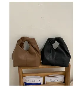 Pair of minimalist pleated leather handbags in brown and black on an artistic wooden stand.