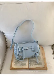 Close-up of a light blue underarm pillow bag with decorative zippers and belt straps