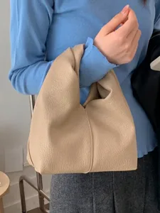 Minimalist beige pleated faux leather slouchy shoulder handbag carried by a model