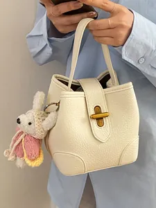 Elegante borsa a mano in pelle crema con chiusura dorata e un tenero ciondolo in peluche