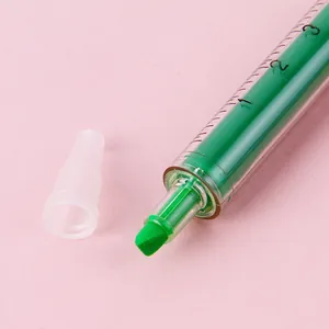 Green syringe-shaped highlighter pen with chisel tip and clear barrel on pink background