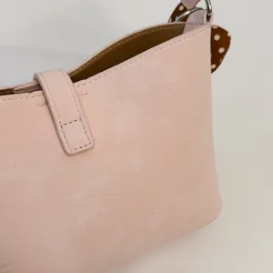 Dettaglio di borsa a spalla in pelle rosa con texture marmorizzata e cuciture fini.