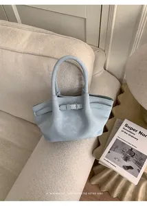 Vista dettagliata di una borsa a mano minimalista azzurra con fibbia su divano crema