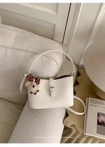 Borsa a secchiello minimalista bianco avorio da donna con ciondolo a orsetto su divano