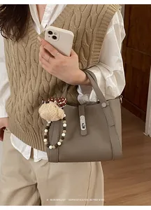Detailweergave van een retro taupe lederen emmer tas met een schattige beer bedeltje.