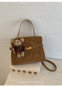 Gros plan d'un sac à main marron vintage avec un charm ours en peluche sur un socle.