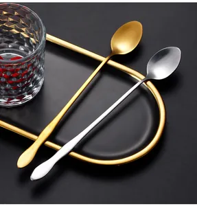 Close-up of long-handled stainless steel spoons in gold and silver finishes on black tray