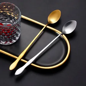 Gold and silver long handle stainless steel mixing spoons displayed on a black tray.