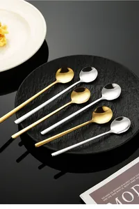 Detailed view of six gold and silver long-handled round stainless steel spoons on a black plate.