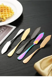 Close-up of multicolored stainless steel butter knives and cream spreaders on dark desk
